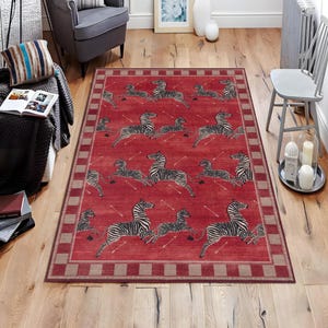 May include: A rectangular red rug with a repeating pattern of zebras in black and white. The rug has a border with a checkered design in shades of red and tan. The zebras are depicted in a running pose.