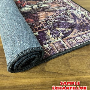 K&ouml;nnte beinhalten: Ein zusammengerollter Teppich mit schwarzem Rand und einer dunkelgrauen R&uuml;ckseite. Der Teppich zeigt ein detailliertes Design einer mythischen Kreatur mit Fl&uuml;geln und einem Vogel. Der Teppich liegt auf einer Holzoberfl&auml;che mit dem in Rot gedruckten Text "SAMPLE &Eacute;CHANTILLON CAMPIONE PROBE".