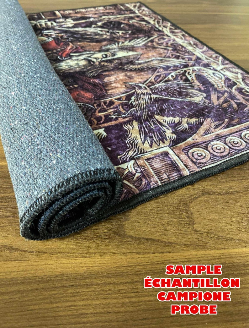 K&ouml;nnte beinhalten: Ein zusammengerollter Teppich mit schwarzem Rand und einer dunkelgrauen R&uuml;ckseite. Der Teppich zeigt ein detailliertes Design einer mythischen Kreatur mit Fl&uuml;geln und einem Vogel. Der Teppich liegt auf einer Holzoberfl&auml;che mit dem in Rot gedruckten Text "SAMPLE &Eacute;CHANTILLON CAMPIONE PROBE".
