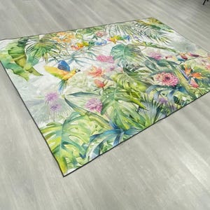 May include: A colorful rug with a tropical theme featuring green leaves, pink flowers, and yellow and blue birds.