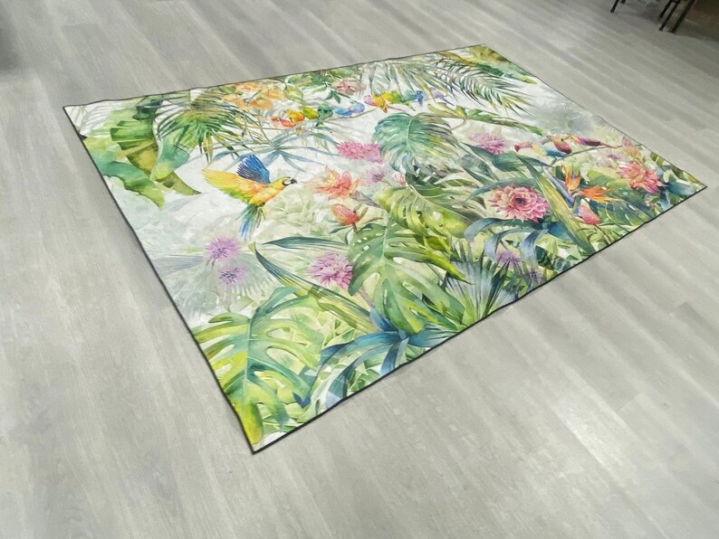 May include: A colorful rug with a tropical theme featuring green leaves, pink flowers, and yellow and blue birds.
