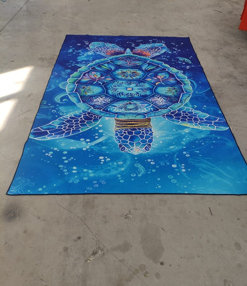 Op de afbeelding: Een blauw en groen mandala-achtig zeeschildpadontwerp op een blauwe achtergrond met witte bubbels. De schildpad heeft een gouden ketting en ingewikkelde details.