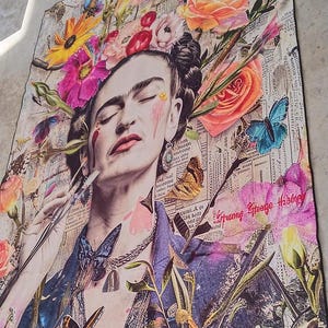 May include: A colorful art print featuring a portrait of a woman with closed eyes, adorned with a floral headdress and butterflies. The artwork incorporates elements of collage, with newspaper clippings and vibrant flowers. The color palette includes pinks, blues, and yellows.