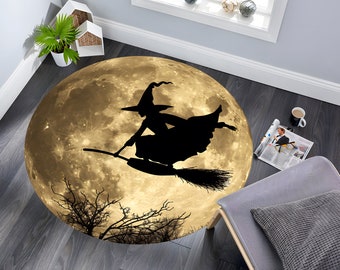 Op de afbeelding: Een rond Halloween-kleed met een silhouet van een heks die op een bezem voor een volle maan vliegt. De maan is goudgeel met een donkerbruine achtergrond.