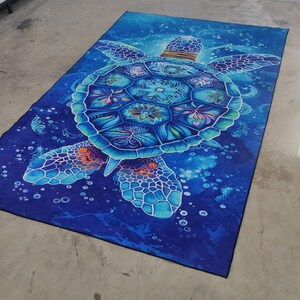 Op de afbeelding: Een blauwe en turquoise zeeschildpad met ingewikkelde patronen op zijn schild, zwemmend in een donkerblauwe oceaan met witte bubbels. Het schild van de schildpad is versierd met bloem- en geometrische patronen.