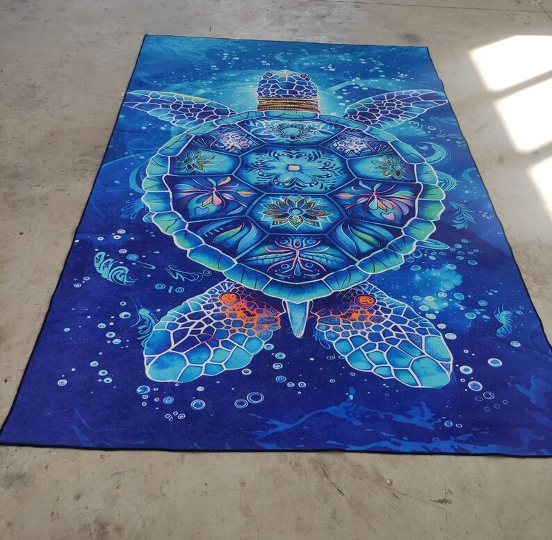 Op de afbeelding: Een blauwe en groene mandala-gepatroneerde zeeschildpad op een blauwe achtergrond met witte bubbels. De schildpad is omringd door een galactisch patroon.