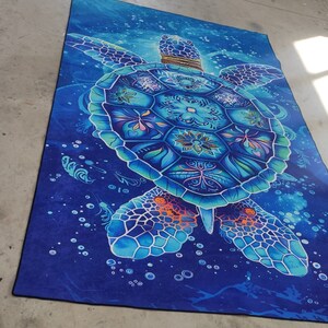 Op de afbeelding: Een blauw en wit mandala-stijl zeeschildpad tapijt met een donkerblauwe achtergrond. De schildpad is omringd door witte bubbels.