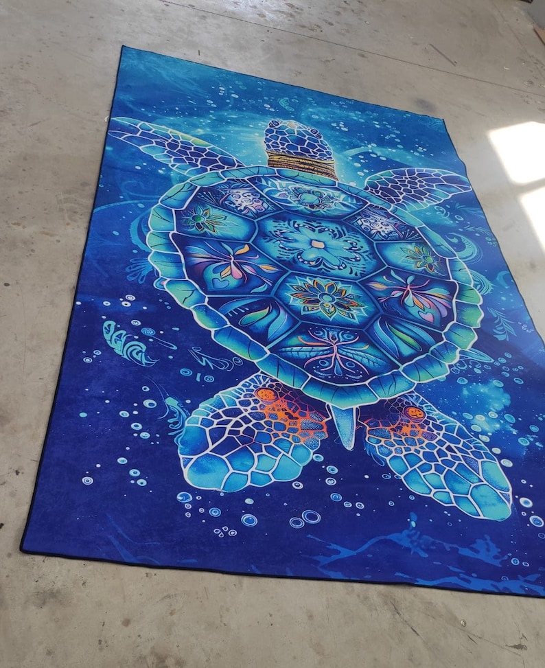 Op de afbeelding: Een blauw en wit mandala-stijl zeeschildpad tapijt met een donkerblauwe achtergrond. De schildpad is omringd door witte bubbels.