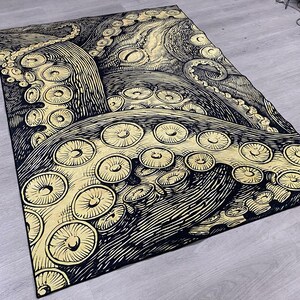 K&ouml;nnte beinhalten: Schwarzer und goldener Teppich mit einem gro&szlig;en Kraken-Design. Die Krakenarme sind mit Saugn&auml;pfen detailliert.