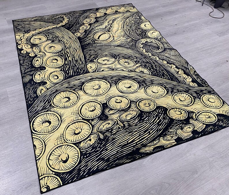 K&ouml;nnte beinhalten: Schwarzer und goldener Teppich mit einem gro&szlig;en Kraken-Design. Die Krakenarme sind mit Saugn&auml;pfen detailliert.