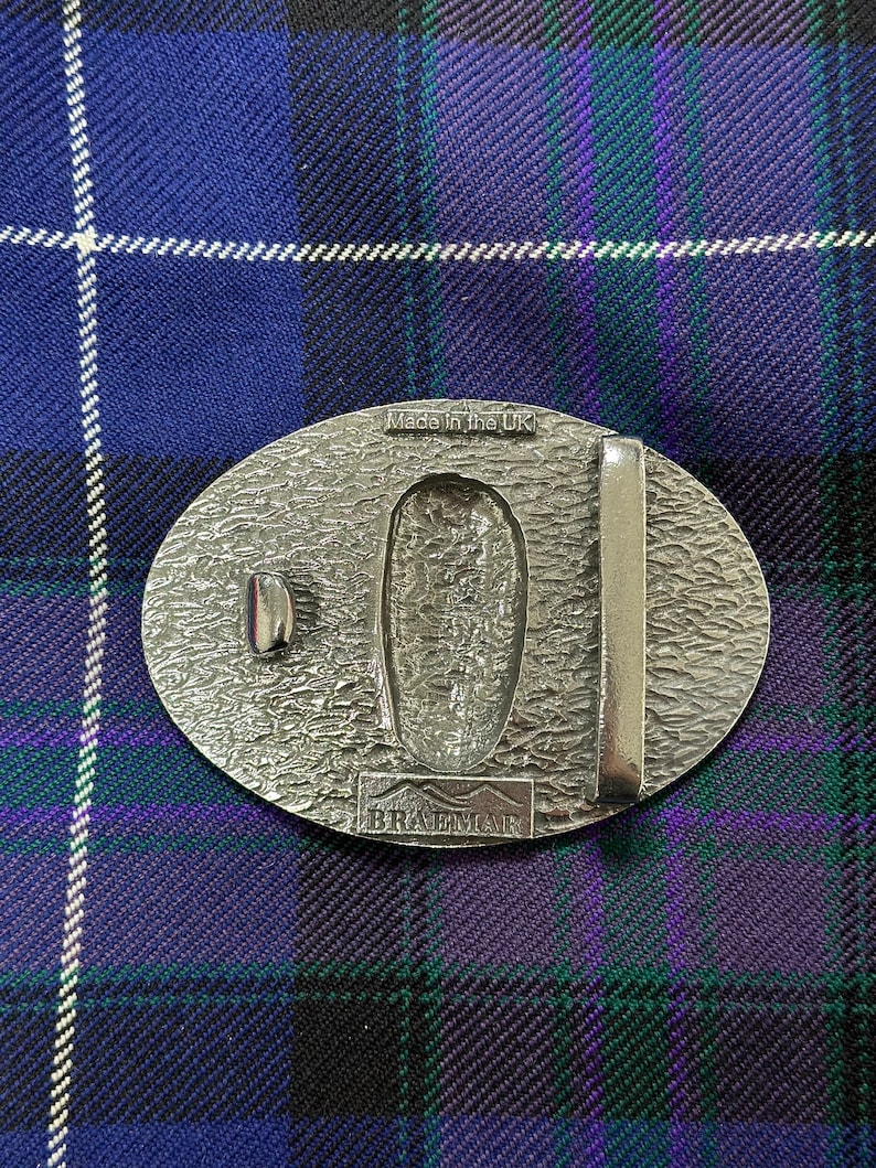 May include: Silver oval belt buckle with a textured surface and the words "Made in the UK" and "Braemar" engraved on it.