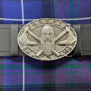 May include: A silver belt buckle with a Viking warrior design. The buckle features a bearded warrior with a helmet and crossed axes. The buckle is surrounded by a circle of runes.