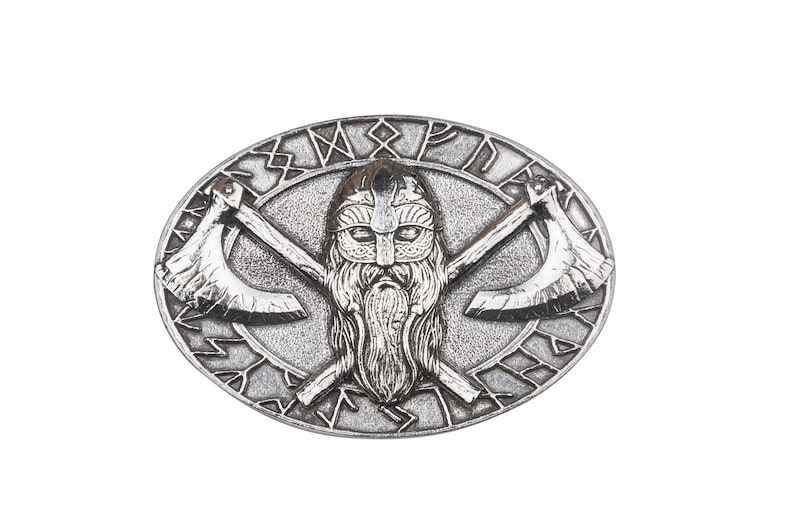 May include: Silver-toned belt buckle with a Viking warrior design. The buckle features a bearded warrior's head with crossed axes and a circular inscription around the edge.