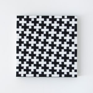 Puede incluir: Arte de pared tejido en blanco y negro con un patrón geométrico. La obra de arte está hecha de tiras de tela que se tejen juntas para crear un diseño a cuadros.