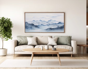 May include: A living room scene featuring a framed watercolor painting of blue mountains. A light-colored sofa with throw pillows sits below the artwork. A wooden coffee table with decorative items and a potted plant complete the room's decor.