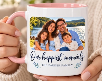 May include: A white ceramic mug with a soft pink interior and handle. The front features a rectangular photo of a family of four near a lake, with the dark blue text "Our happiest moments" and "THE PARKER FAMILY" printed below.