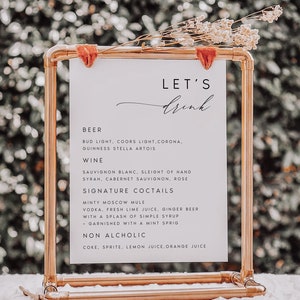 May include: A copper pipe frame holds a white sign with a handwritten menu for a wedding or party. The sign reads "Let's Drink" and lists beer, wine, signature cocktails, and non-alcoholic options.