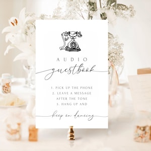 May include: A white sign with black text and a black and white illustration of a rotary phone. The sign reads "AUDIO guestbook" and includes instructions for using the phone as a guest book: "1. PICK UP THE PHONE 2. LEAVE A MESSAGE AFTER THE TONE 3. HANG UP AND keep on dancing"