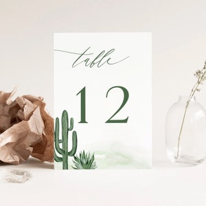 May include: A white card with green watercolor cactus illustrations and the text "table 12" printed in green.