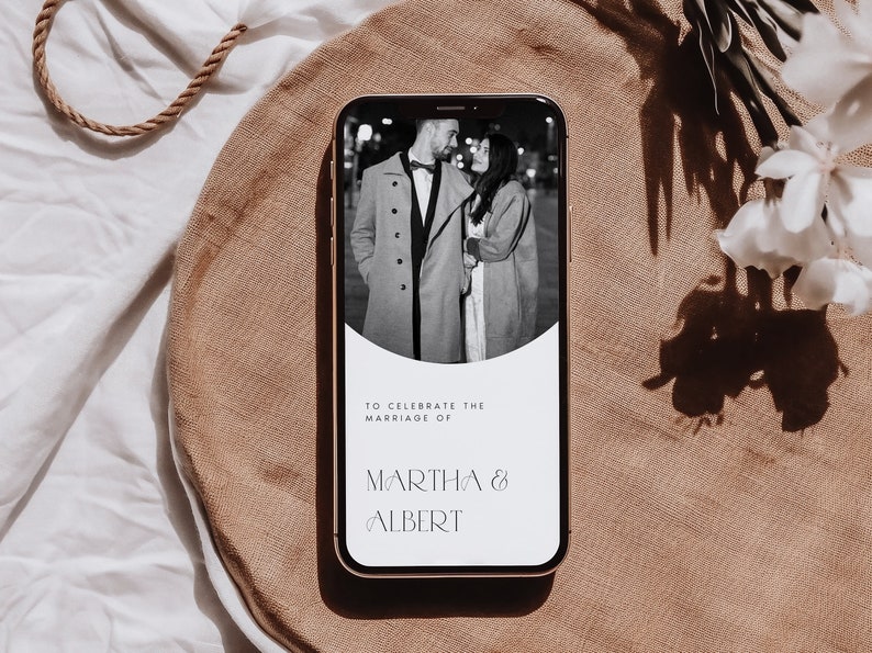 Op de afbeelding: Een smartphone-scherm toont een huwelijksuitnodiging met een zwart-witfoto van een stel op de achtergrond. De tekst luidt "Ter gelegenheid van het huwelijk van Martha & Albert".