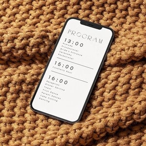 Op de afbeelding: Een smartphone die een huwelijksprogramma weergeeft met de tijden en gebeurtenissen van de dag. De telefoon ligt op een bruin gebreid deken.