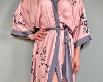 May include: A long pink satin robe with a floral print and a gray trim. The robe has a tie belt and a front opening.