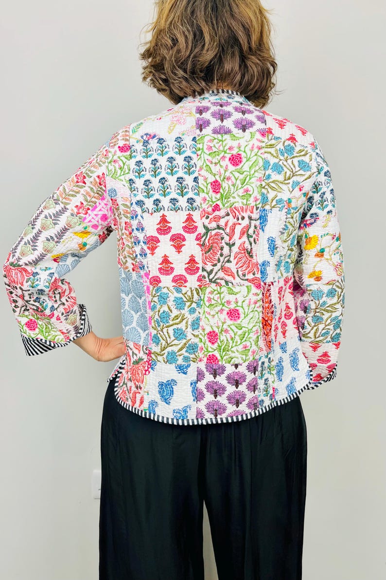 Pu&ograve; includere: Una giacca trapuntata bianca con un design a patchwork che presenta motivi floreali in vari colori, tra cui rosa, blu, verde e viola. La giacca ha un colletto alla coreana e maniche lunghe.
