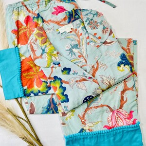 May include: A light blue pajama set with a floral print and turquoise trim. The set includes a long-sleeved top with a collar and pants with a drawstring waist.