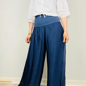 以下が含まれることがあります： 白いボタンダウンのクロップドブラウスにウエストにリボンをつけた女性が、濃い青色のワイドレッグパンツを履いています。