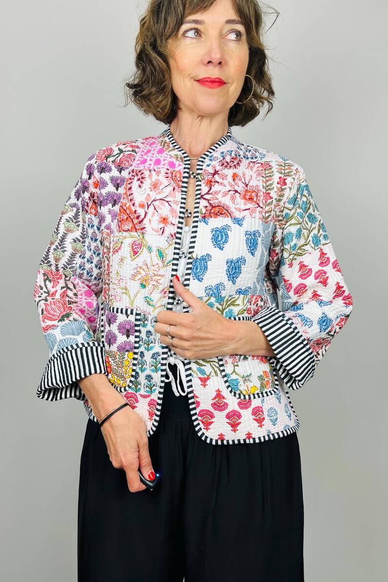 Pu&ograve; includere: Una giacca trapuntata bianca con un design a patchwork che presenta motivi floreali e paisley in tonalit&agrave; di rosa, blu, verde e rosso. La giacca ha un colletto alla coreana, una chiusura a cravatta e bordi a righe bianche e nere.