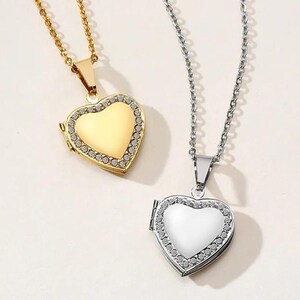 Pode incluir: Dois colares com pingentes em forma de coração. Um é dourado com uma corrente dourada e uma borda de pequenos cristais transparentes. O outro é prateado com uma corrente prateada e uma borda de cristal semelhante. Ambos estão fechados.