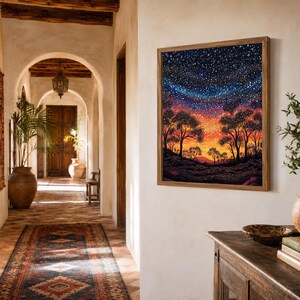 May include: A square framed painting hanging on a wall, depicting a landscape at twilight with silhouettes of trees against a vibrant orange and yellow horizon that transitions into a deep blue night sky filled with numerous white stars.