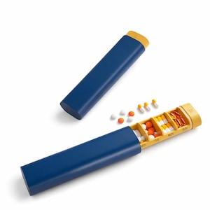 May include: A blue and yellow pill organiser with a sliding lid. The organiser is open, revealing compartments labelled for each day of the week, filled with various pills and capsules. Several loose pills are scattered nearby.
