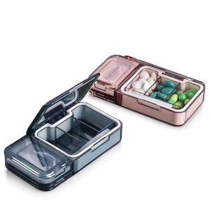 Könnte beinhalten: Zwei Pillen-Organizer, einer offen und einer geschlossen. Der offene Organizer ist dunkelgrau mit einem transparenten Deckel und zeigt drei Fächer. Der geschlossene Organizer ist roségoldfarben, ebenfalls mit drei Fächern, gefüllt mit weißen und grünen Pillen.