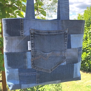 Könnte beinhalten: Eine Patchwork-Denim-Tragetasche in verschiedenen Blautönen. Die Tasche hat eine Vordertasche und zwei Denim-Griffe. Ein kleines weißes Etikett mit Text ist sichtbar. Handgefertigtes Produkt.