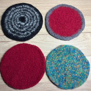 Könnte beinhalten: Vier runde Filzuntersetzer in verschiedenen Farben. Einer ist schwarz und grau mit einem Spiralmuster, ein anderer ist rot mit einem grauen Rand, ein dritter ist einfarbig rot und der letzte ist blau und grün mit einem gesprenkelten Muster.