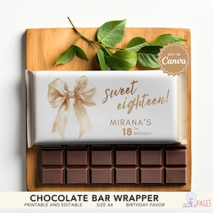 Può includere: Una barretta di cioccolato con un involucro bianco con un fiocco dorato e la scritta "Sweet eighteen!" con un nome e un compleanno. La barretta è su un vassoio di legno con foglie verdi.