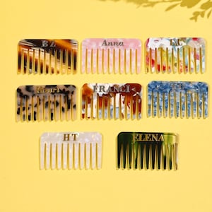 May include: A selection of personalized combs in diverse colours and patterns, such as tortoiseshell, pink, floral, and blue. Each comb has a name or initials in a gold font. The combs are displayed on a yellow surface.