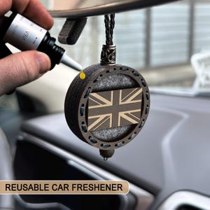 Könnte beinhalten: Ein runder Auto-Lufterfrischer aus Holz mit Union Jack-Flaggen-Design. Der Erfrischer ist dunkelbraun mit einer hellbraunen Flagge und einer schwarzen Kordel zum Aufhängen. Der Text "REUSABLE CAR FRESHENER" steht unten.