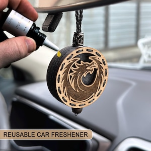 May include: A reusable car air freshener with a dragon design. The round, wooden freshener is dark brown with a lighter brown dragon carving. A black cord and a small bead hang from the bottom. The text "REUSABLE CAR FRESHENER" is at the bottom.