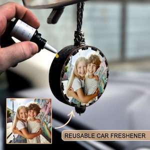 May include: A black, round reusable car air freshener with a photo of two smiling children. The freshener is hanging from a braided black cord. The text "REUSABLE CAR FRESHENER" is visible.