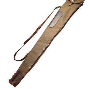 May include: A brown and green canvas and leather gun case with a shoulder strap. The case has a leather flap closure with a buckle and a leather patch on the side. The case is designed to hold a long gun.