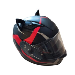 Może przedstawiać: Czarny kask motocyklowy z czerwonymi i białymi akcentami i czarnymi uszami kota. Kask ma przezroczysty wizjer.