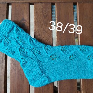 Könnte beinhalten: Eine türkisblaue Stricksocke mit einem Spitzenmuster. Die Socke ist mit "38/39" gekennzeichnet.