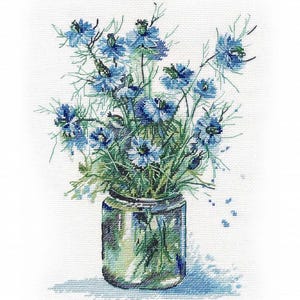 Può includere: Un mazzo di fiori selvatici blu in un vaso di vetro trasparente. I fiori hanno petali delicati e steli lunghi. Il vaso è su uno sfondo bianco.