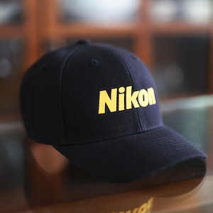 May include: A black baseball cap with a yellow "Nikon" logo.