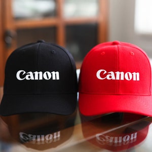 May include: Two baseball caps, one black and one red, both with the word "Canon" embroidered in white on the front.