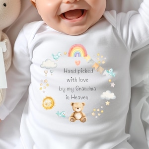 May include: White baby onesie with a watercolor design featuring a rainbow, birds, clouds, stars, and a teddy bear. The text reads "Hand picked with love by my Grandma in Heaven."