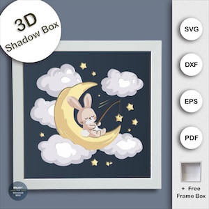 May include: A framed 3D shadow box art piece featuring a whimsical scene. A light brown bunny sits on a yellow crescent moon, fishing for gold stars. White clouds and stars are scattered against a dark blue background. The text "3D Shadow Box" is in a white circle.