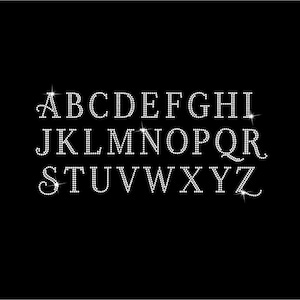 Op de afbeelding: Een compleet alfabet van A tot Z in hoofdletters, opgebouwd uit kleine, reflecterende witte strass-steentjes tegen een effen zwarte achtergrond. Elke letter heeft een elegante schreeflettertype-stijl met een sprankelend effect.